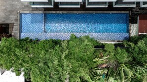 A modern building with a large rectangular pool surrounded by lush greenery. - The Capital Hotel and Resort Seminyak (Keroboken Kelod)