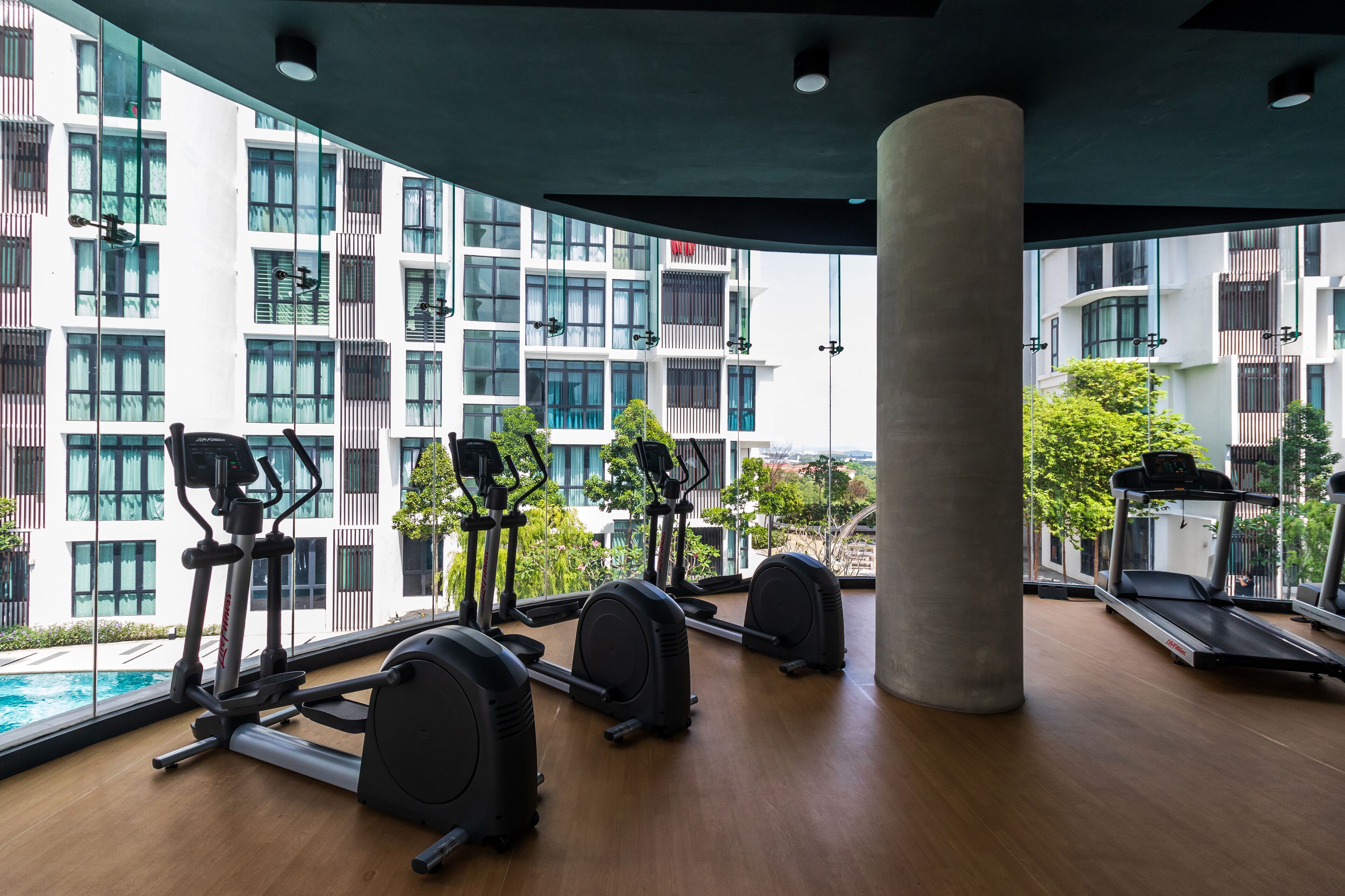 A modern gym with various exercise equipment, large windows, and a view of a residential building.