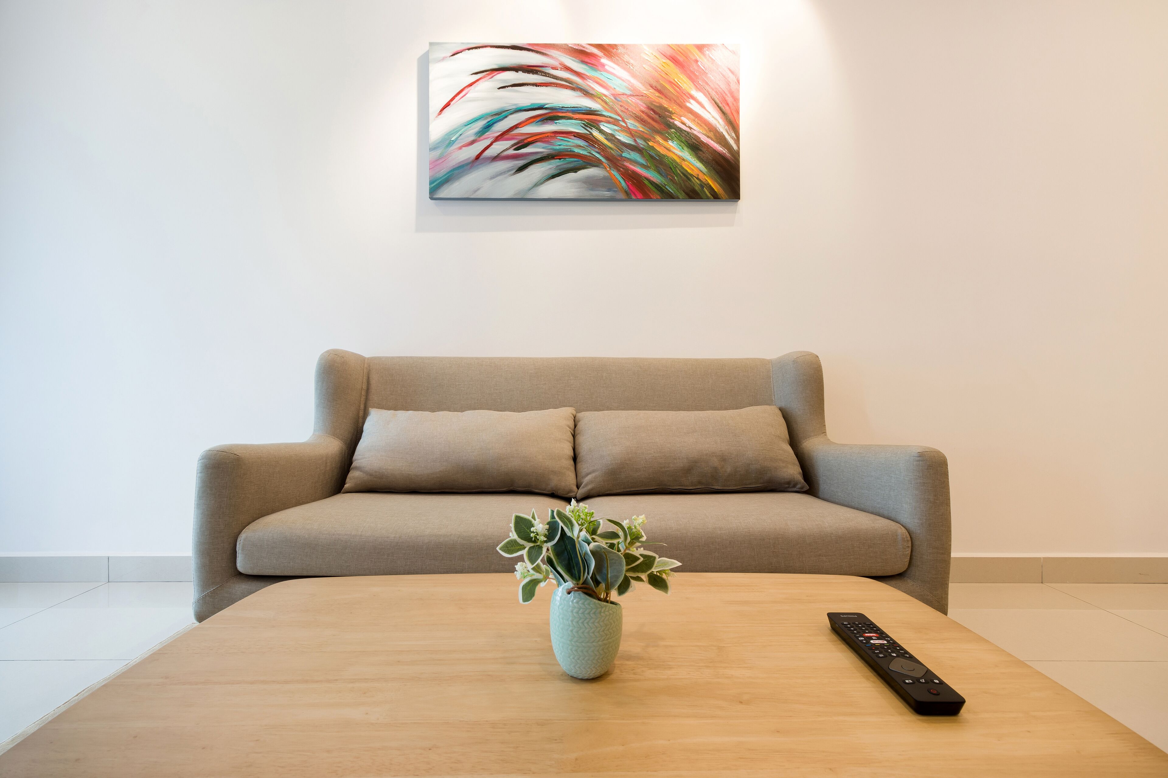 A living room with a beige sofa, a wooden coffee table with a plant and a remote control.