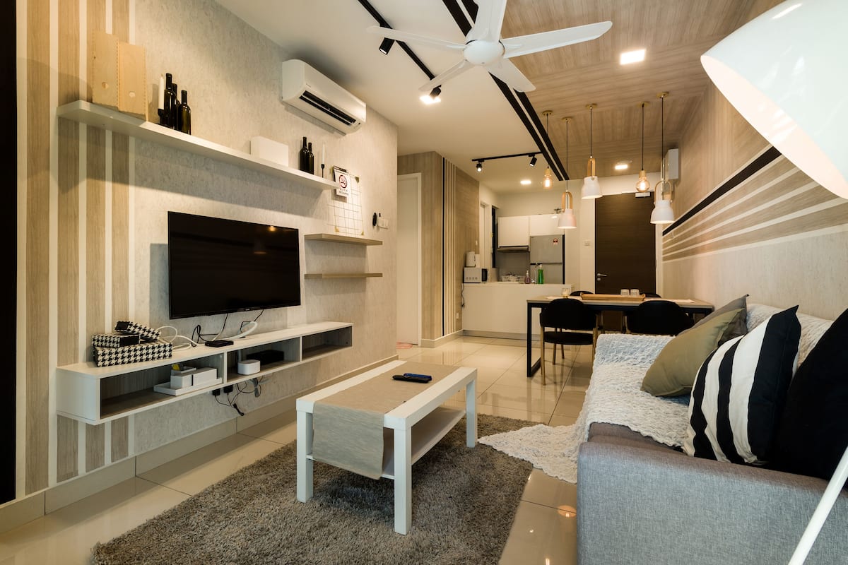 A modern living room with a flat-screen TV, white coffee table, and a sofa with striped cushions.