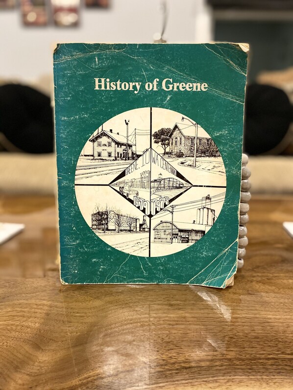 A book titled "History of Greene" with a vintage design, placed on a wooden surface. - Charming home now with access to the Shell Rock River.<br> (Greene)