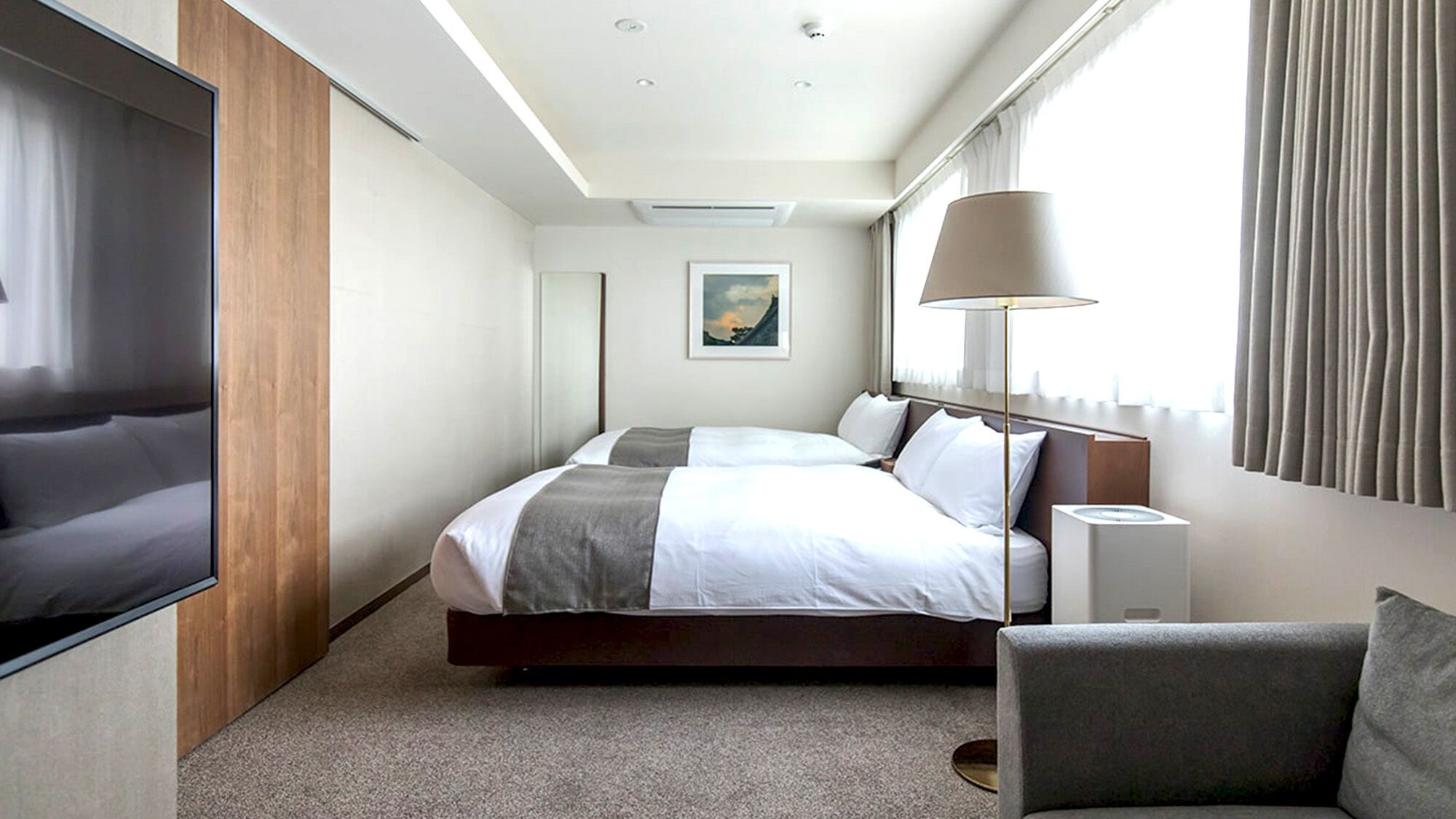 A hotel room with a bed, a TV, a lamp, a painting, and a window with curtains.