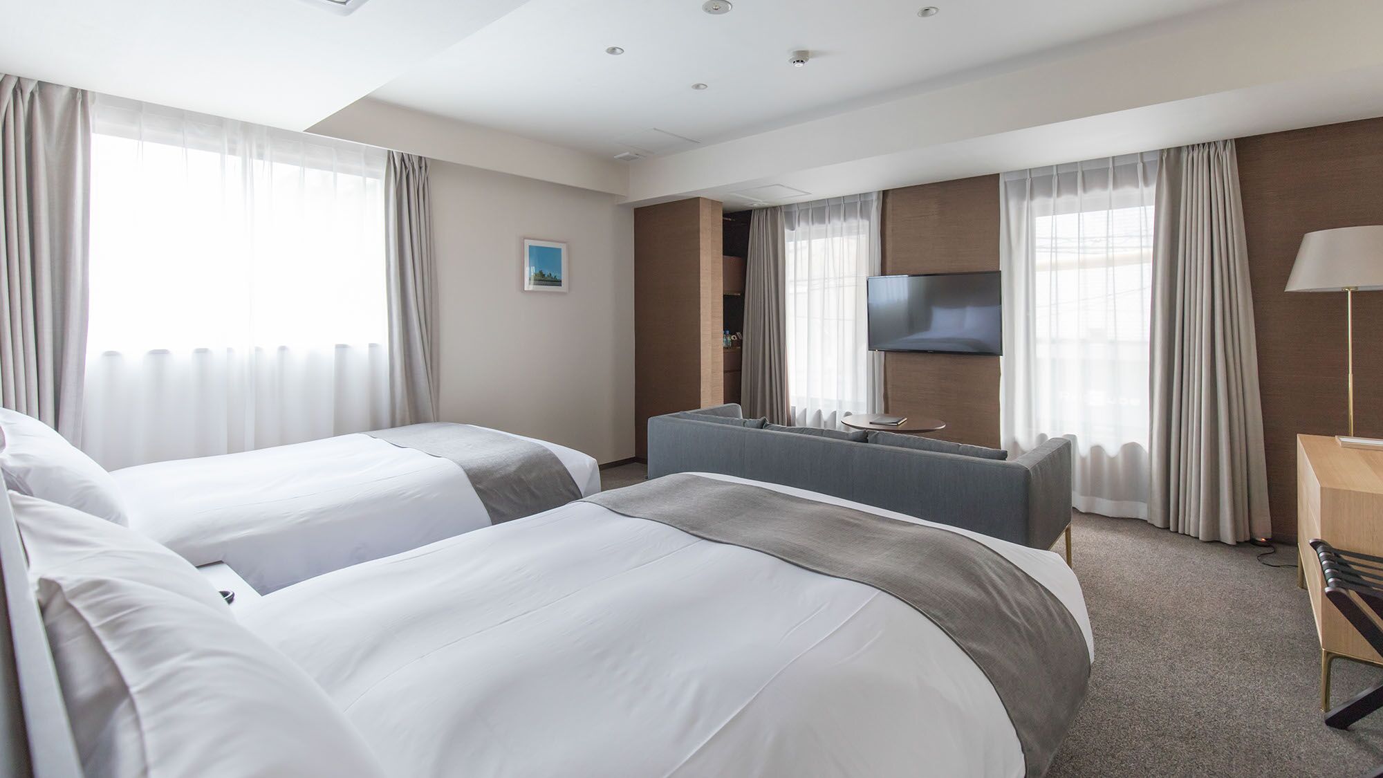 A hotel room with two beds, a desk, a TV, and a lamp.