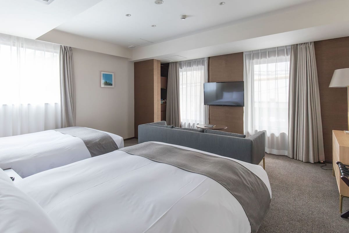 A hotel room with two beds, a desk, a TV, and a lamp.