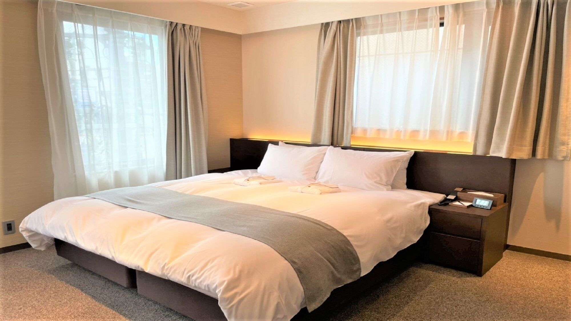 A hotel room with a large bed, two bedside tables, a nightstand, and a window with curtains.