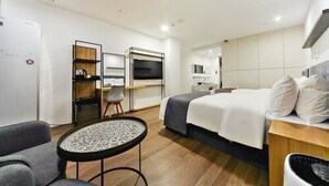 A modern hotel room with a bed, a desk, a chair, a small round table, and a TV.