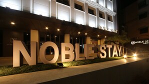 The exterior of a hotel with large illuminated signage reading "NOBLE STAY".
