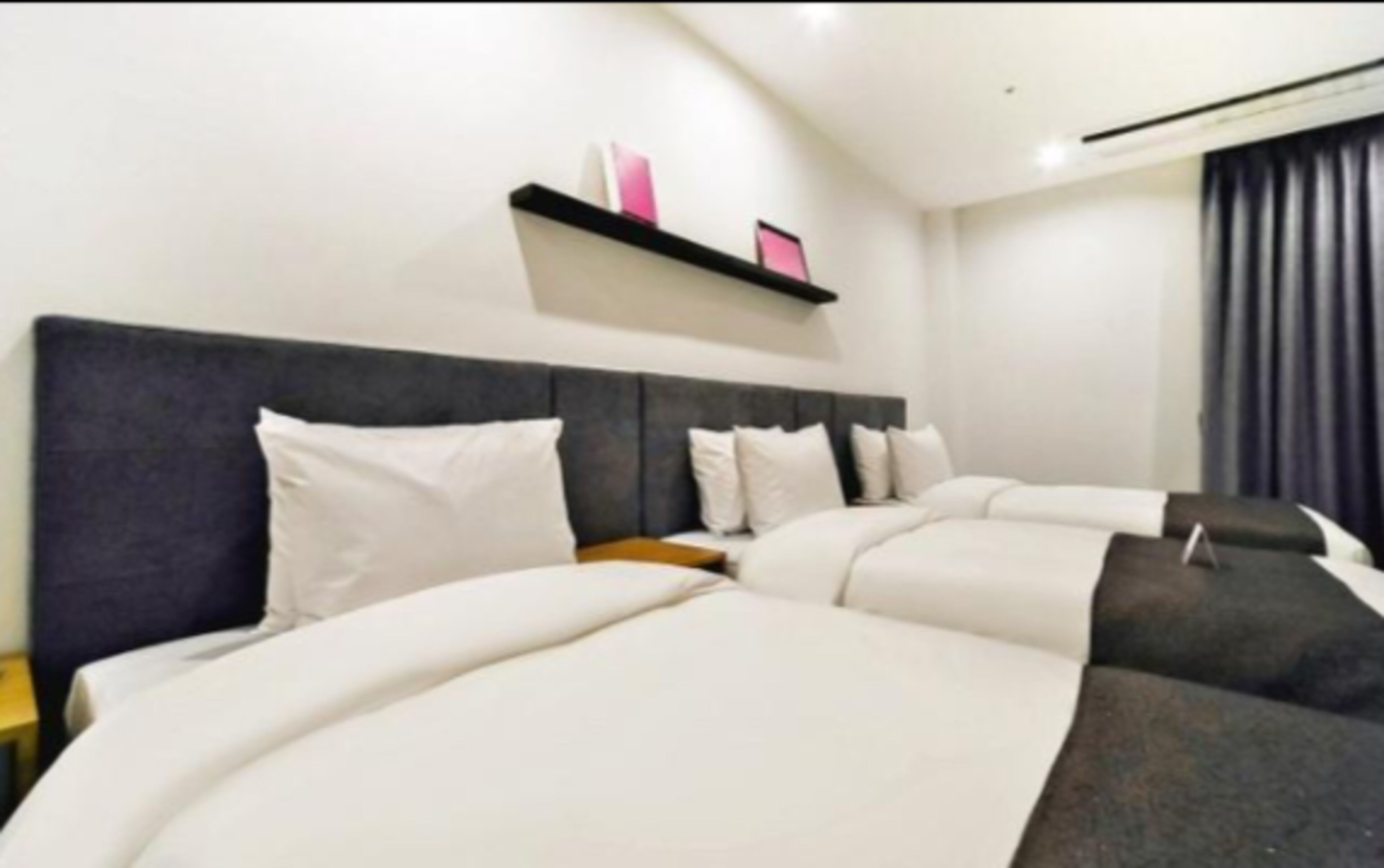 Habitación de hotel con una cama grande, un cabecero, una repisa con objetos y una ventana con cortinas.