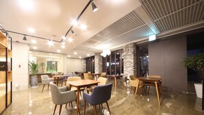 A modern cafe with wooden tables and chairs, large windows, and a polished floor.