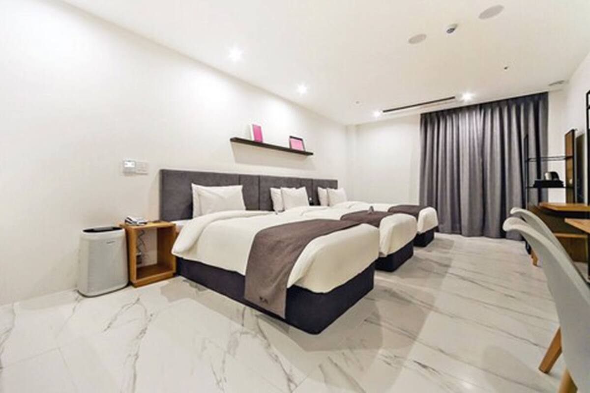 Habitación de hotel con dos camas, un escritorio, una silla, un cesto de basura y un amplio ventanal con cortinas.