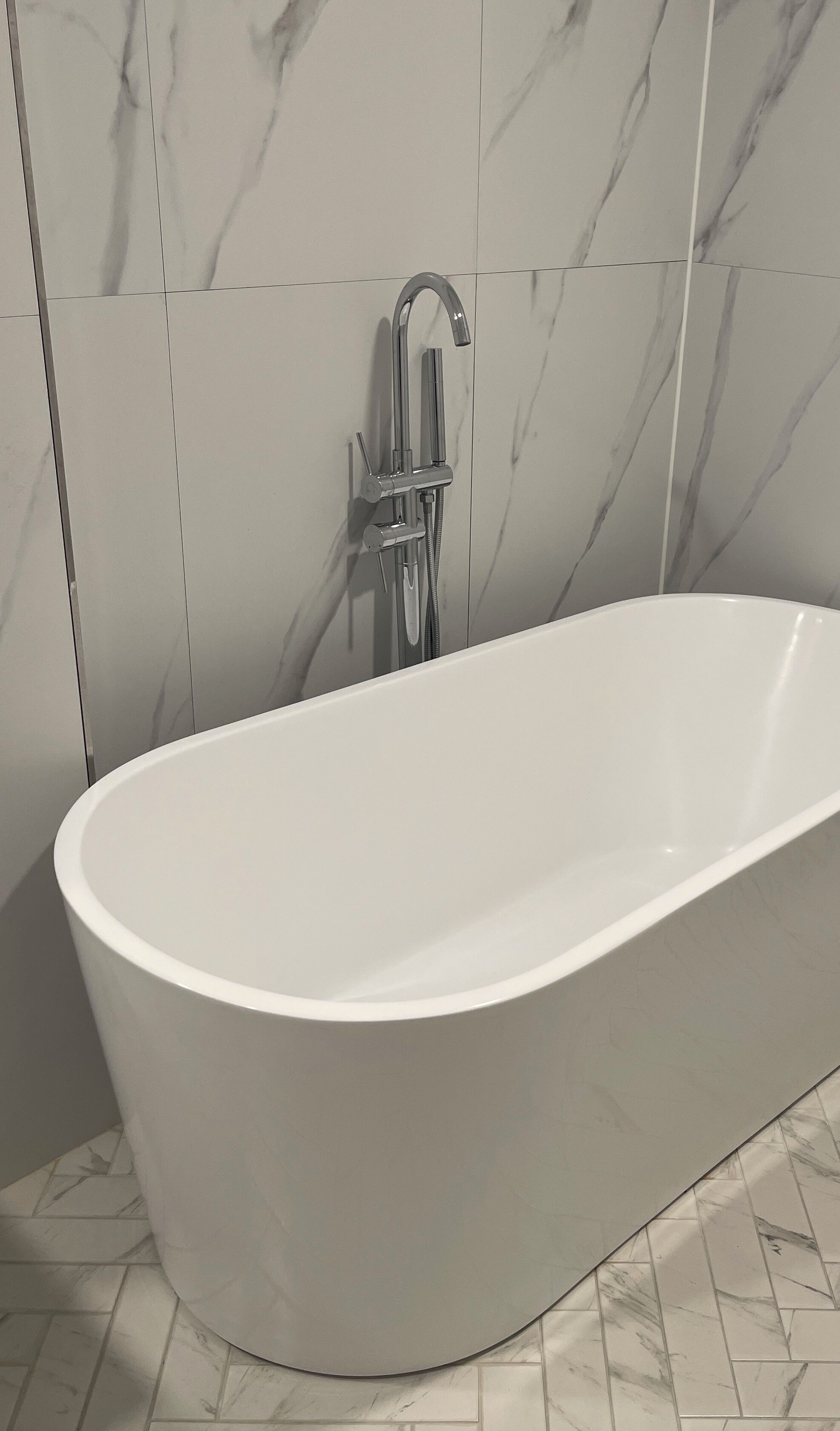 A modern bathroom with a freestanding bathtub, a wall-mounted showerhead, and marble-patterned tiles.
