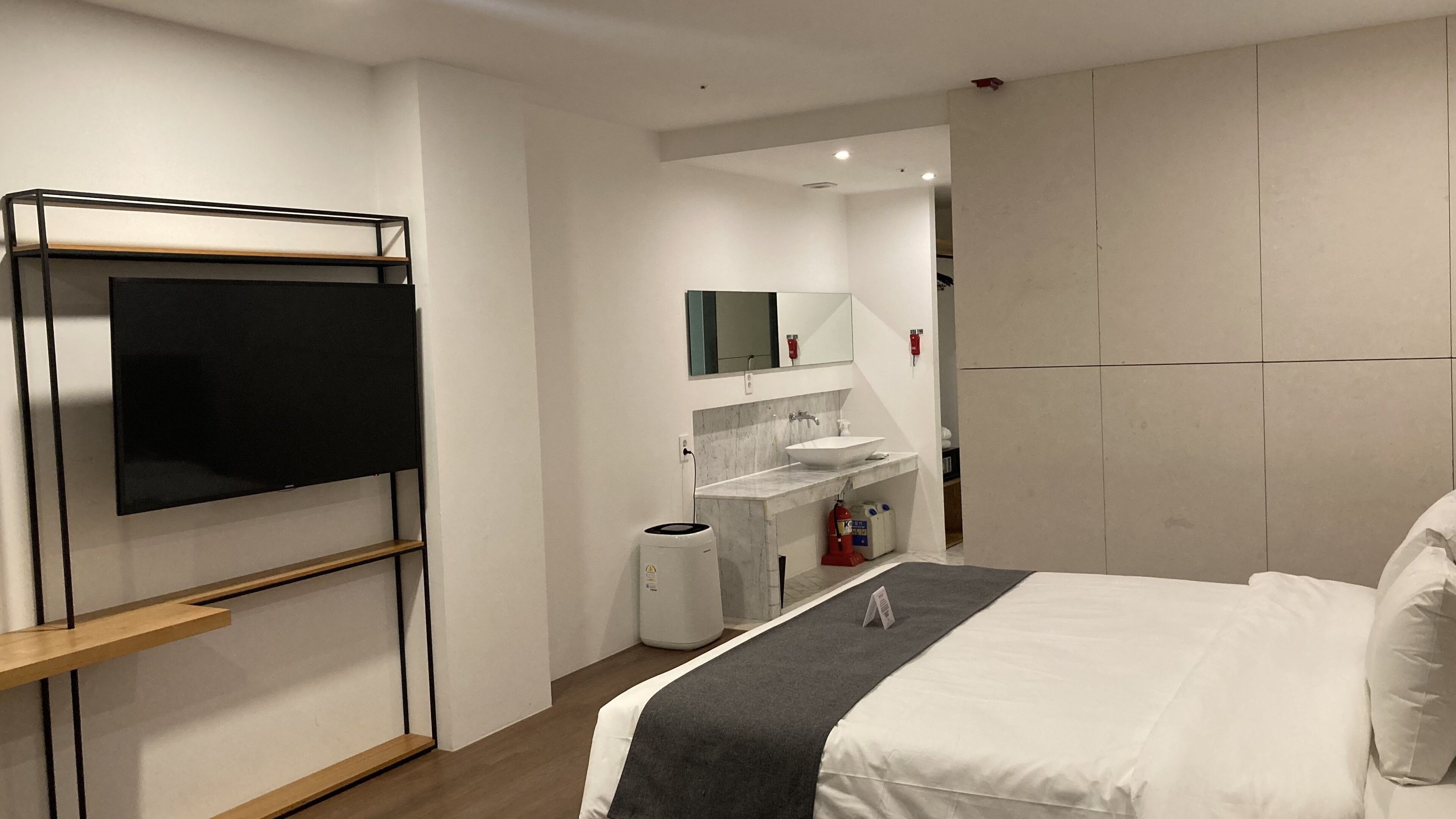 A hotel room with a bed, a TV mounted on a wall, a bathroom with a sink and mirror, and a wardrobe.