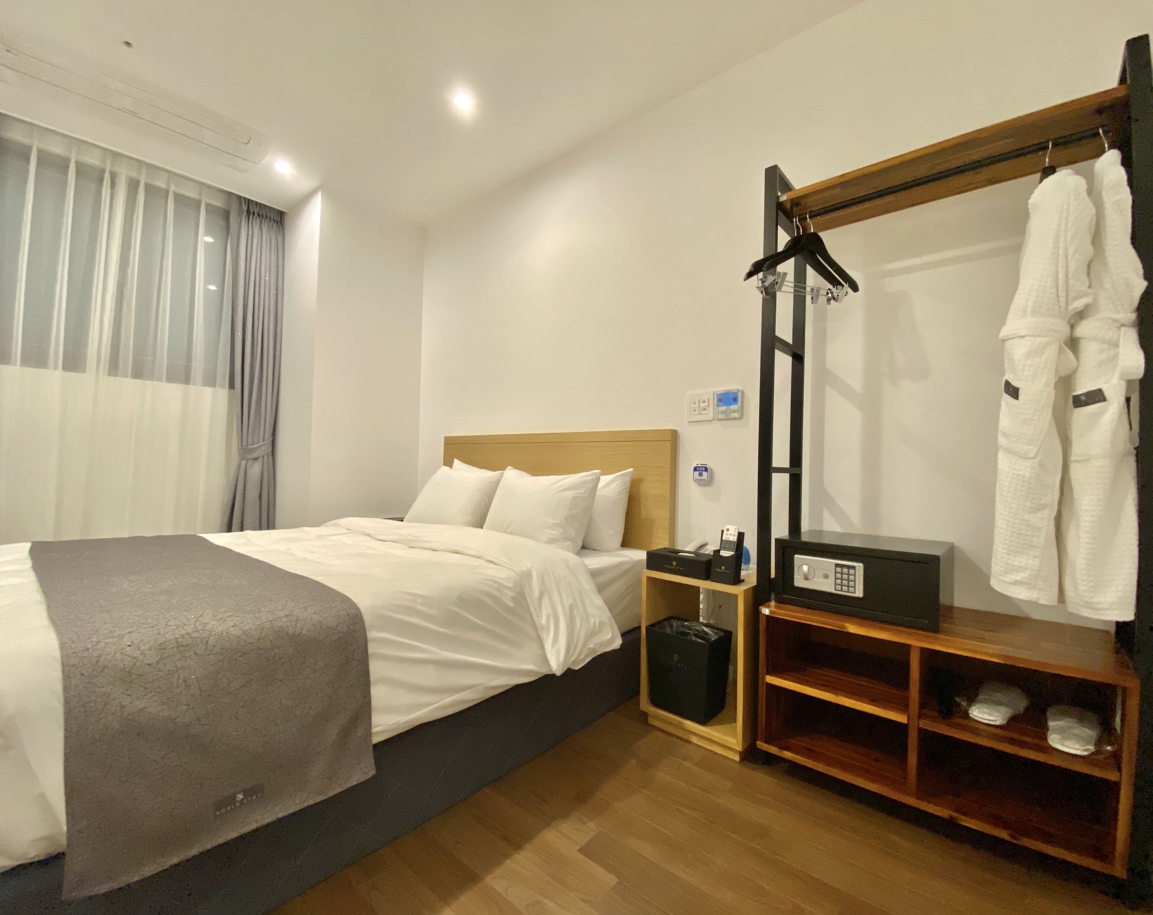 Una habitación de hotel con cama, mesita de noche y perchero para bata.