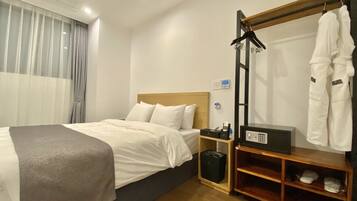 Una habitación de hotel con cama, mesita de noche y perchero para bata.