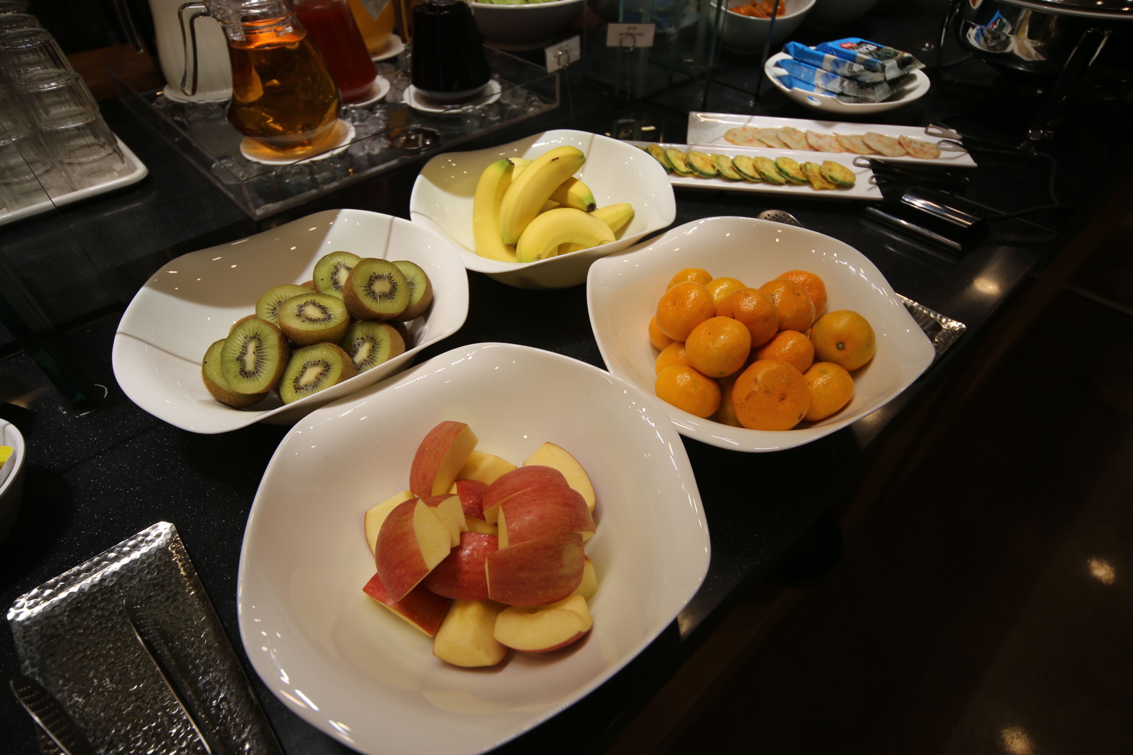 A buffet table with various fruits including kiwi, apples, bananas, and oranges.
