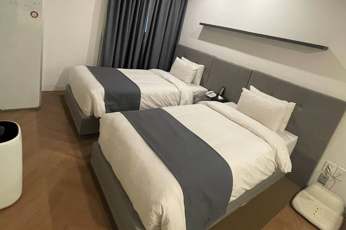 Habitación de hotel con dos camas, una mesita de noche, un teléfono y un estante en la pared.
