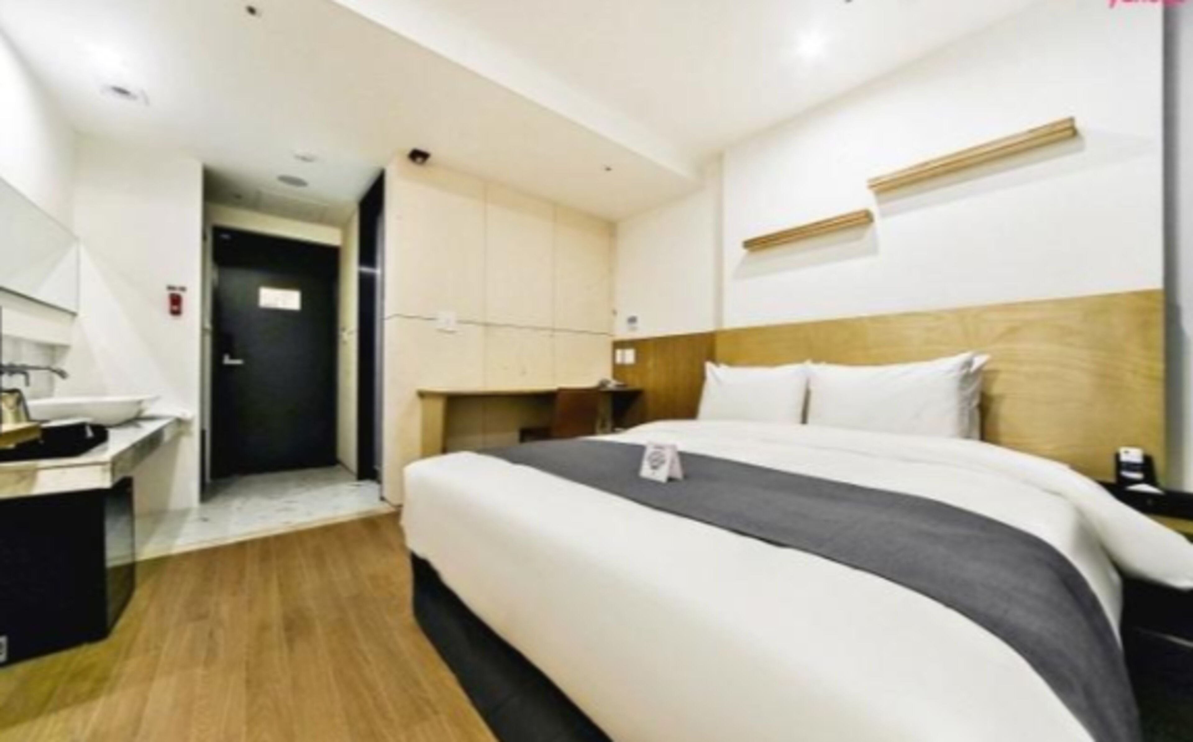 A hotel room with a bed, bedside table, and a small desk with a chair.