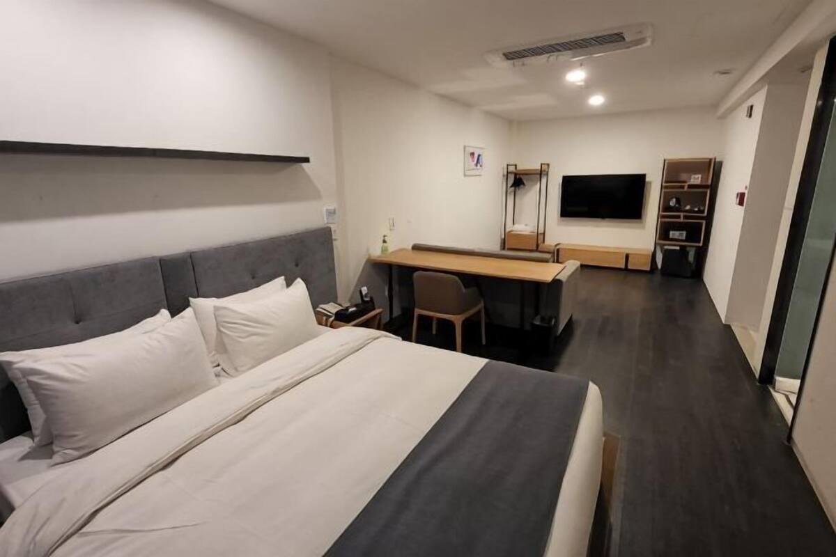 Habitación de hotel con cama, escritorio, silla, televisor y armario.