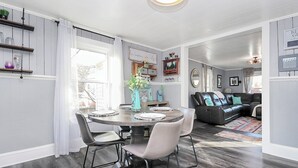 A dining area with a round table, chairs, and a vase of flowers. There is a couch and a rug in the background. - Lake Norman Shabby Chic bungalow in Cornelius close to Davidson (Cornelius)