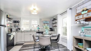 A modern kitchen with grey cabinets, a central island, and a dining area with a round table and chairs. - Lake Norman Shabby Chic bungalow in Cornelius close to Davidson (Cornelius)
