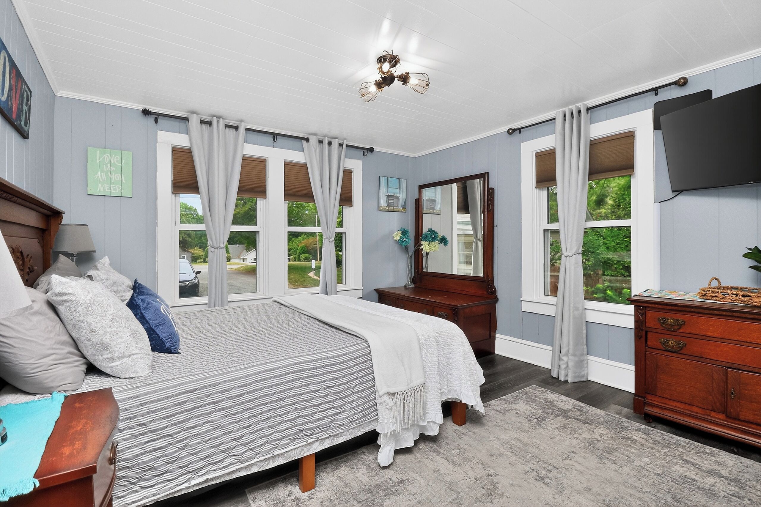 Une chambre à coucher avec un lit, une commode, un miroir et de grandes fenêtres.