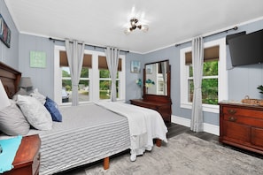 Un dormitorio con cama, cómoda, espejo y ventanas amplias.