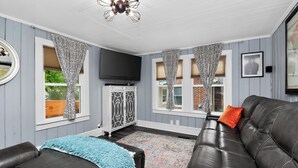 A living room with a black leather sofa, a television, and patterned curtains. - Lake Norman Shabby Chic bungalow in Cornelius close to Davidson (Cornelius)