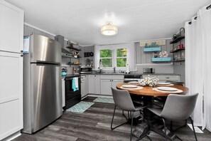 Una cocina moderna con un refrigerador de acero inoxidable, una mesa de comedor de madera con sillas y una ventana con cortinas.