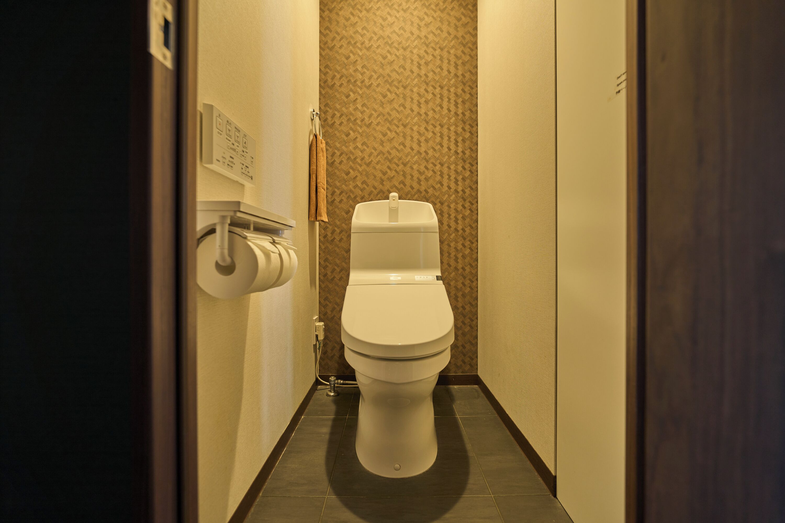 Un pasillo estrecho que lleva a un baño con pared estampada y una toalla colgada.