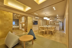 Een moderne hotelkamer met een houten vloer, een zithoek met een tafel en stoelen, een kitchenette met een magnetron en koelkast, en een aan de muur bevestigde televisie.