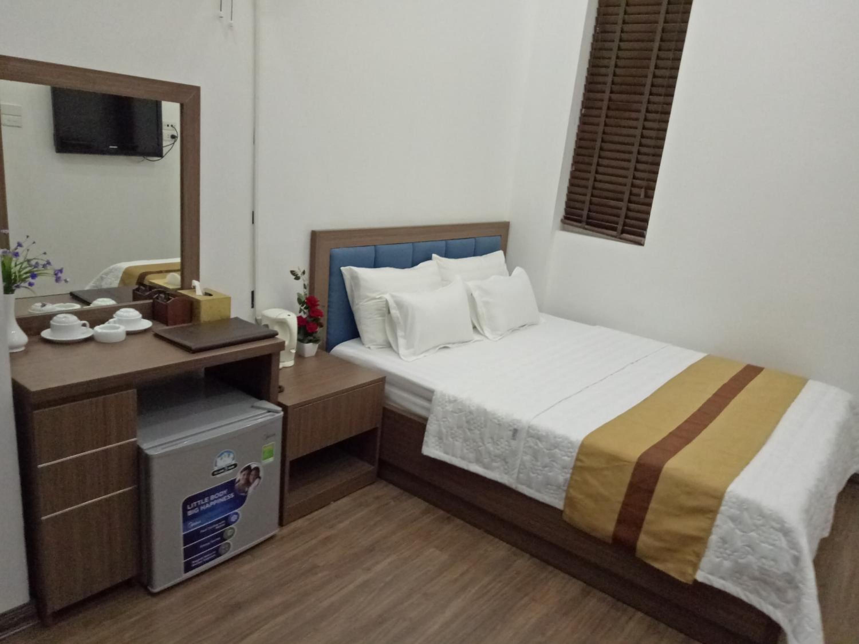 Habitación de hotel con cama, escritorio con computadora, espejo y ventana con persianas.