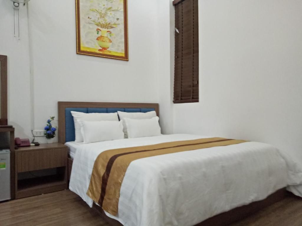 A bedroom with a bed, a nightstand, a lamp, a painting, and a window with blinds.