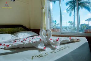 A hotel room with a bed featuring a towel arrangement spelling "MEMENTO" and a view of palm trees and the ocean. - Memento Resort (Ngapali)