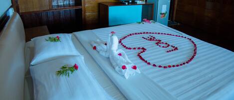 A neatly made bed with a heart-shaped arrangement of rose petals, a white towel, and a decorative swan.
