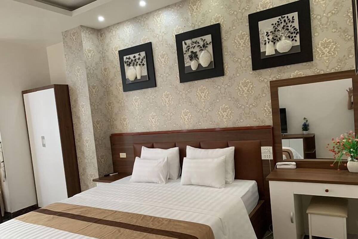 A hotel room with a large bed, a desk, and a mirror. There are three framed pictures on the wall.
