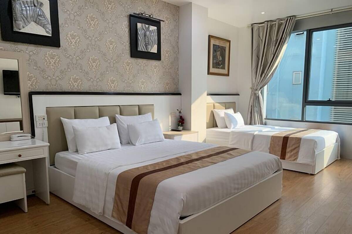 A hotel room with two beds, a large window with curtains, and a wall with framed artwork.
