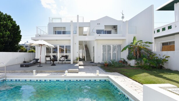 Una casa moderna de dos pisos con piscina, mobiliario exterior y un jard ín bien cuidado.