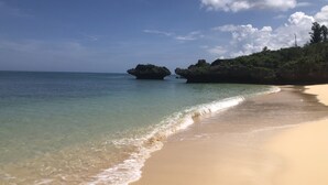 Una playa con aguas cristalinas, arena dorada y afloramientos rocosos.
