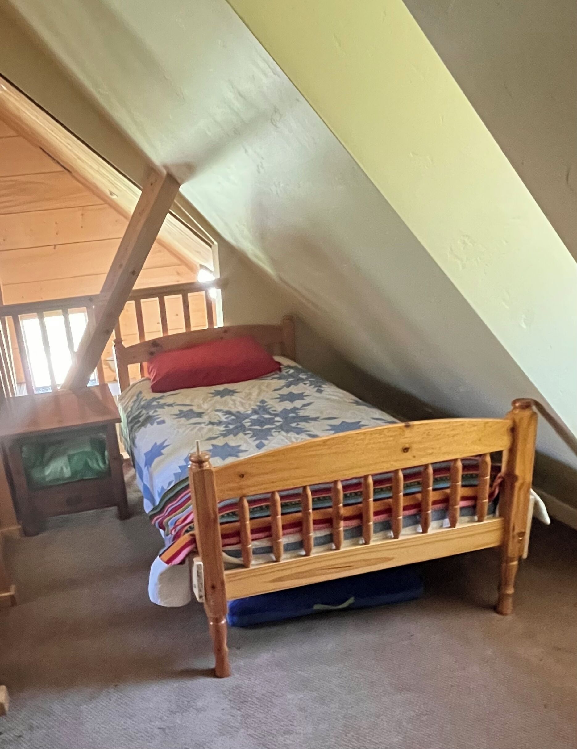 Een kleine kamer met een enkel bed, schuine wanden, een houten hoofdbord en een kleurrijk beddegoed.