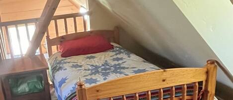 Een kleine kamer met een enkel bed, schuine wanden, een houten hoofdbord en een kleurrijk beddegoed.