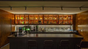 A bar area with a long counter, multiple shelves of liquor bottles, and three bar stools. - glue Hotel (Seoul)