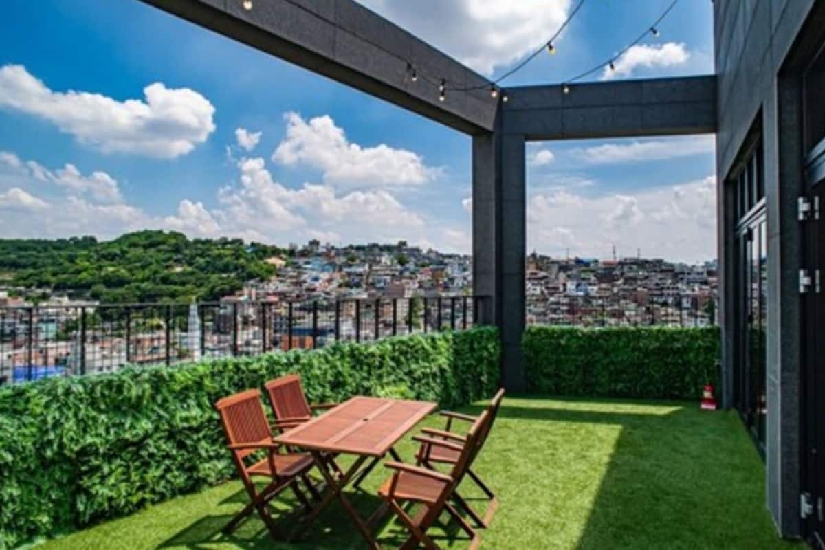 An outdoor patio with a table and chairs, a view of a cityscape, and a hedge.