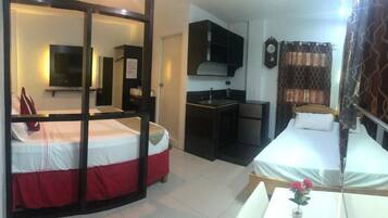A compact hotel room with a bed, a small kitchenette, a TV, and a mirror.
