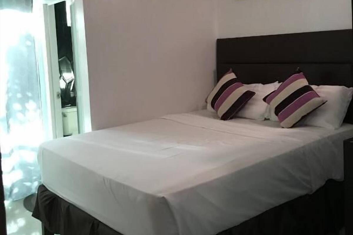 Une chambre à coucher avec un lit, une tête de lit sombre et deux tableaux floraux accrochés au mur.