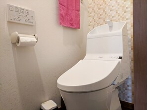 A bathroom with a toilet, a paper towel dispenser, and a tiled wall. - Grato Terrace (Tokyo)