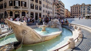 Una plaza pública con una fuente grande, rodeada de edificios históricos y una multitud de personas.