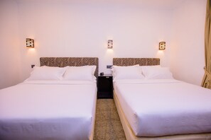Ein Hotelzimmer mit zwei Betten, jeweils mit einem gemusterten Kopfteil, weißer Bettwäsche und Wandleuchten.