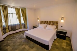 Ein Hotelzimmer mit einem großen Bett, zwei Nachttischen, einem Kopfteil mit Zebra-Muster und einem Fenster mit Vorhängen.