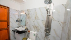 A bathroom with a marble floor, a white sink, a toilet, a shower, and a wooden door. - Huddle (Nuwara Eliya)