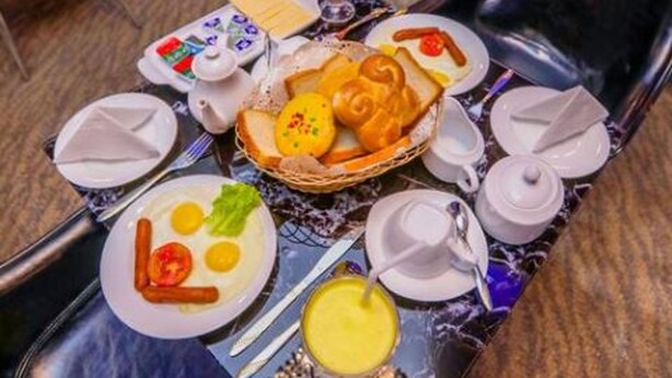 A breakfast buffet with various dishes, including eggs, toast, and fruit, set on a table with black chairs and a patterned table runner. - Huddle (Nuwara Eliya)